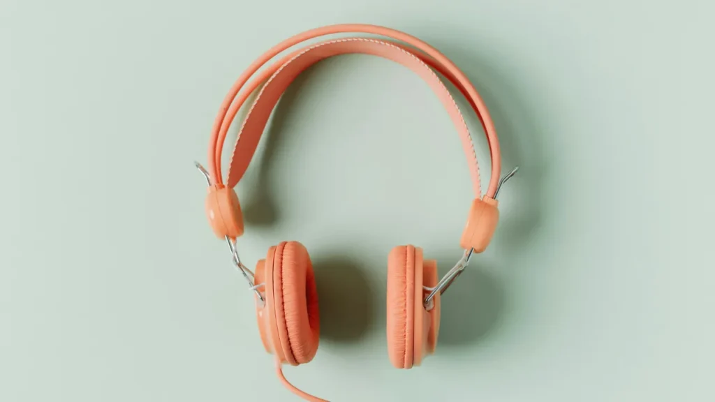 Wired Headphones Are Back Coral-colored wired headphones on a mint green background, viewed from above