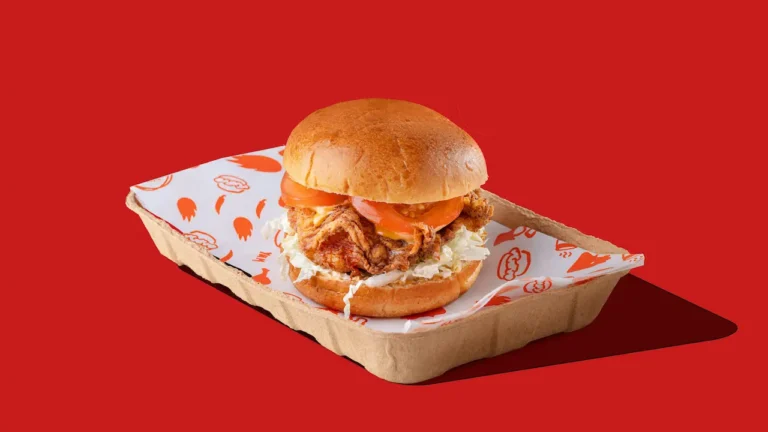 Crispy chicken burger with tomato and slaw in a cardboard tray on a bright red background, styled like a fast food ad.