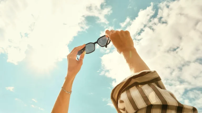 8:10 PM Person holding sunglasses up toward a bright summer sky, used in a C1 lesson plan on how to have a great summer.