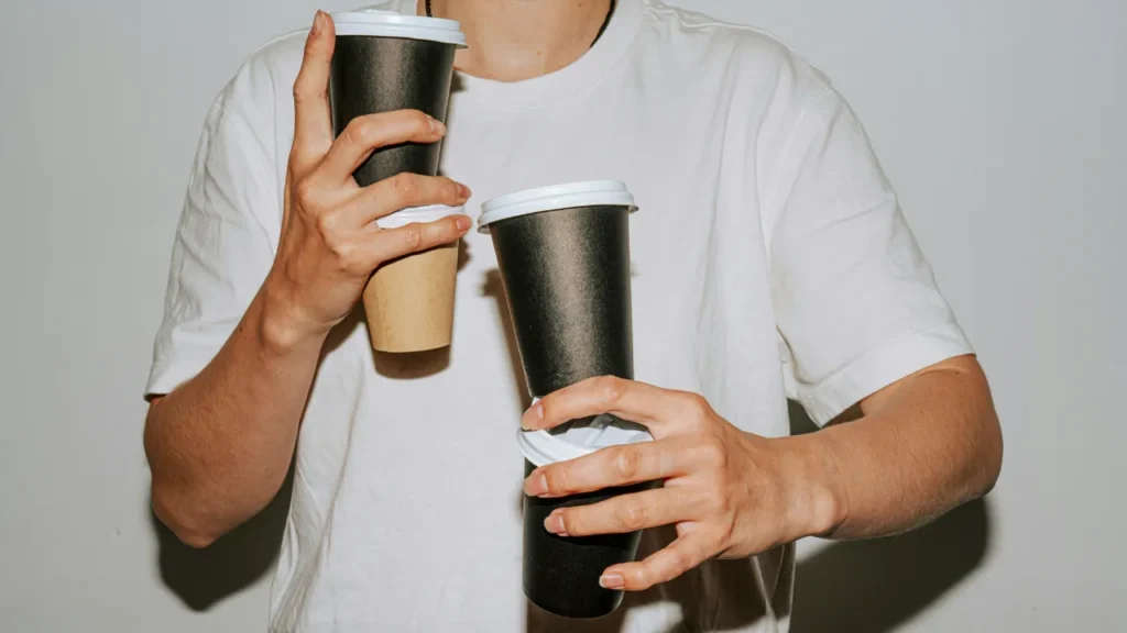 How to Quit Coffee Person holding three takeaway coffee cups at once, illustrating caffeine dependency in a C1 lesson plan on quitting coffee.