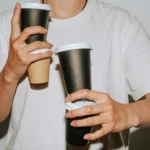 Person holding three takeaway coffee cups at once, illustrating caffeine dependency in a C1 lesson plan on quitting coffee.