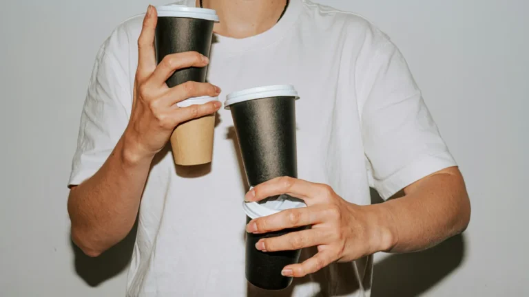 Person holding three takeaway coffee cups at once, illustrating caffeine dependency in a C1 lesson plan on quitting coffee.