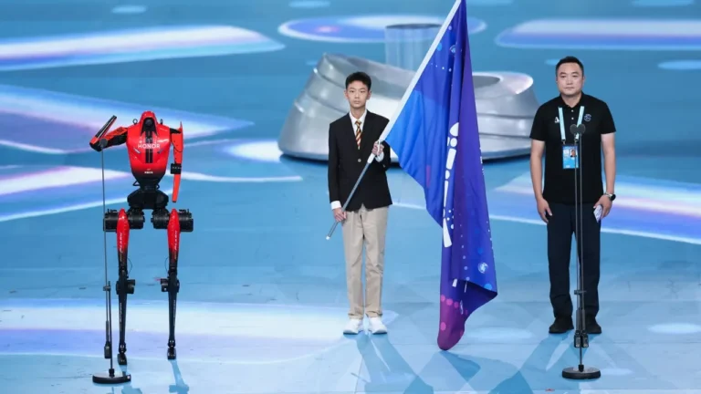 Red humanoid robot stands beside a flag bearer at China's Robot Games, a lesson plan robots topic for ESL classes